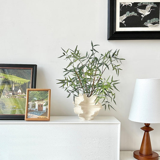Ruffled wave ceramic vase displayed with decorative branches on a sideboard