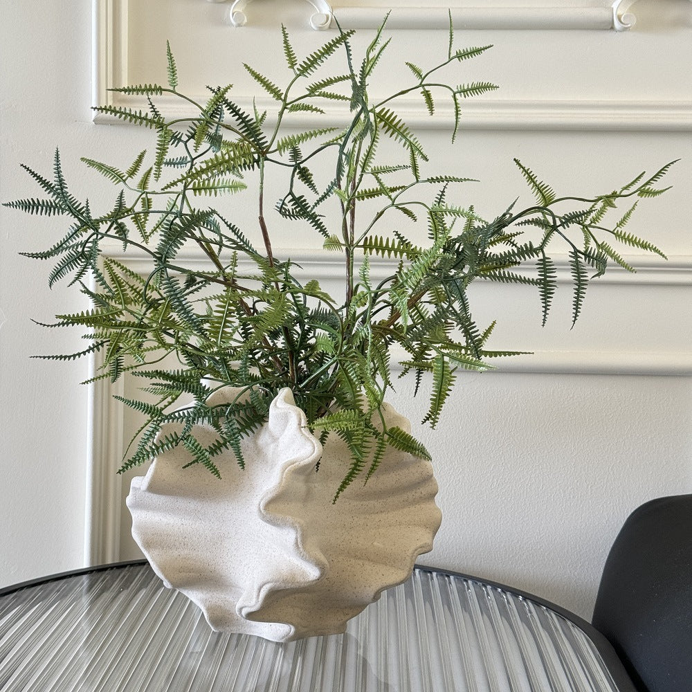 Ruffled wave ceramic vase displayed with decorative branches on a table